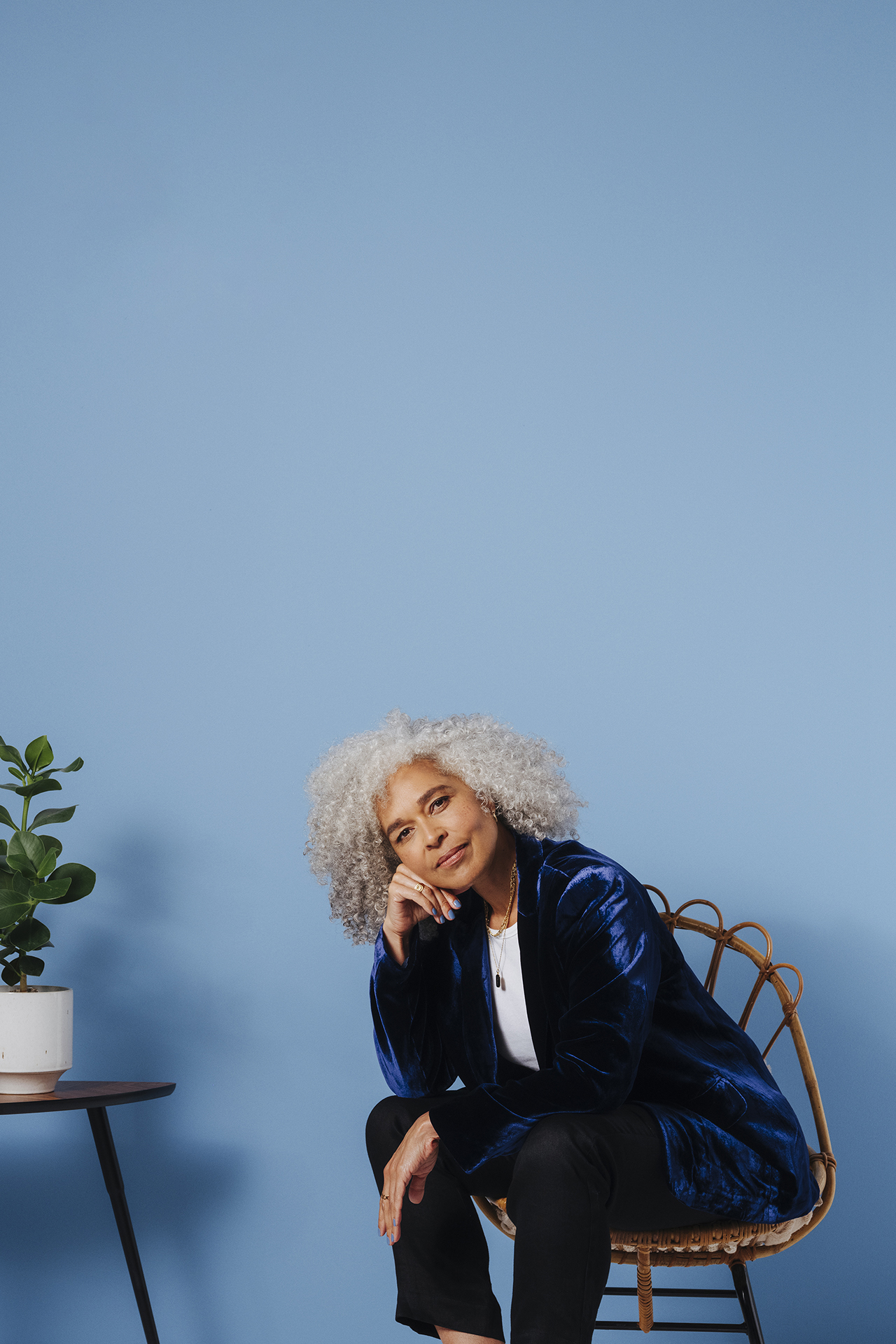 woman sat next to side table with plant in front of blue wall